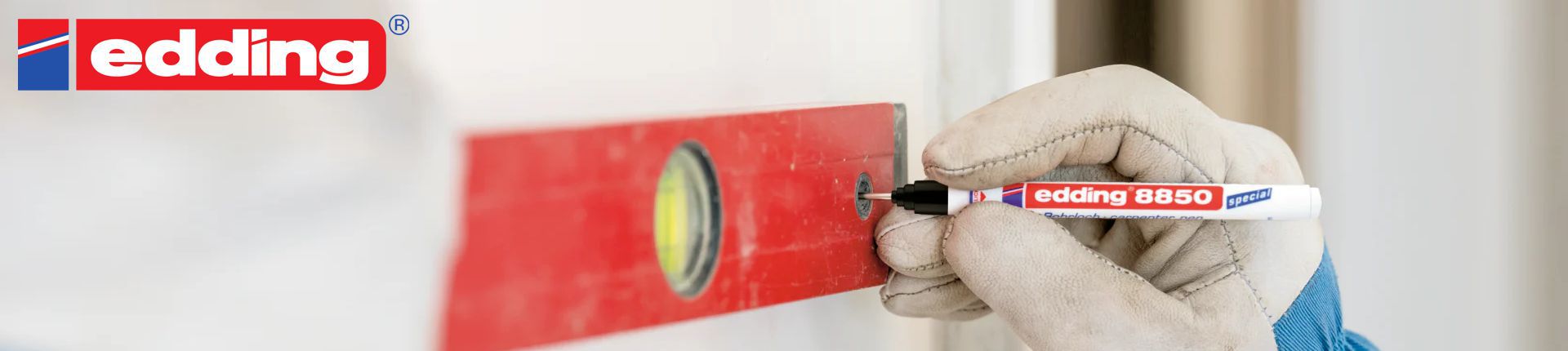 Bild Special Edding im Einsatz beim Anzeichnen einer Markierung an einer beige-grauen Wand mit Hilfe einer roten Wasserwaage