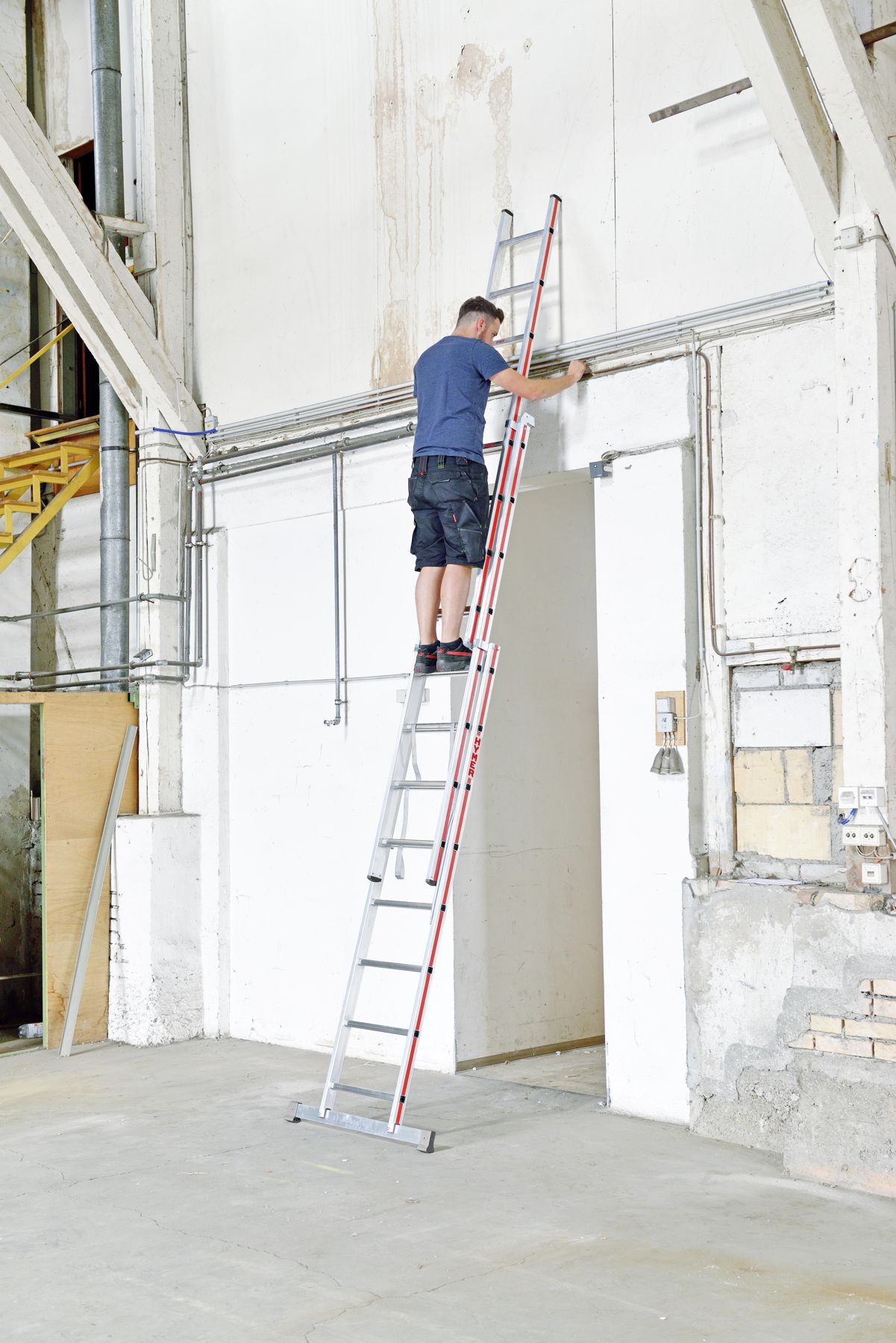 Handwerker auf einer dreiteiligen Mehrzweckleiter von Hymer stehend bei Arbeiten an einer wandmontierten Leitung bild 3