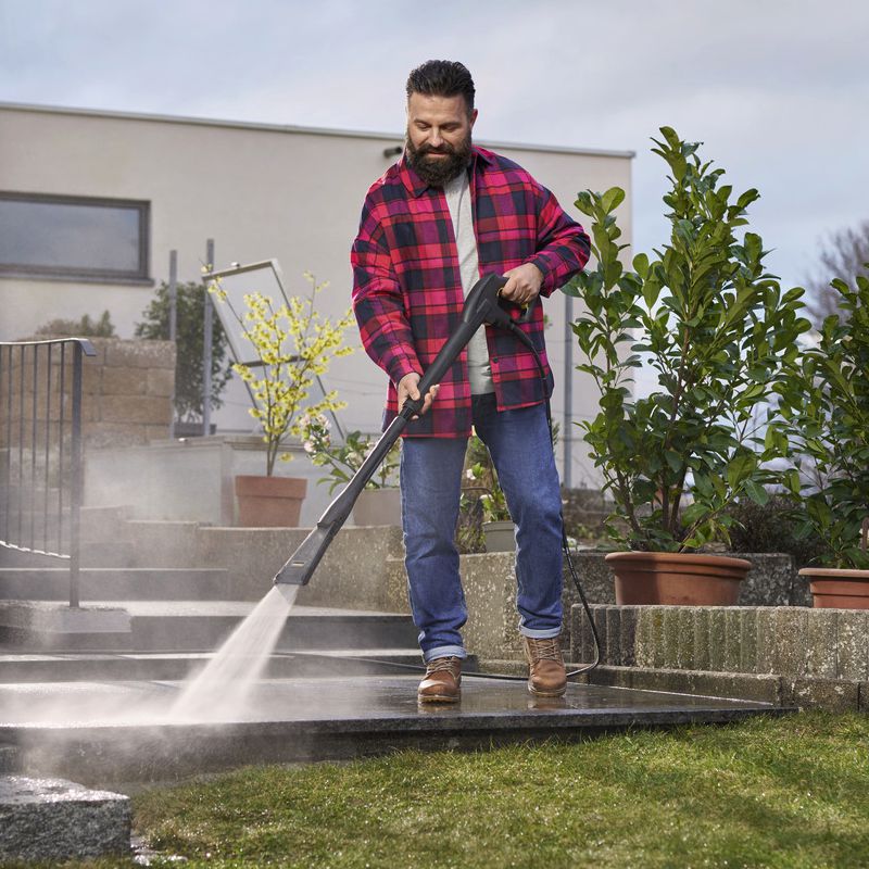 Mann mit dunklem Bart und dunklen kurzen Haaren reinigt eine Steinterrasse mit einem Kärcher eco Booster