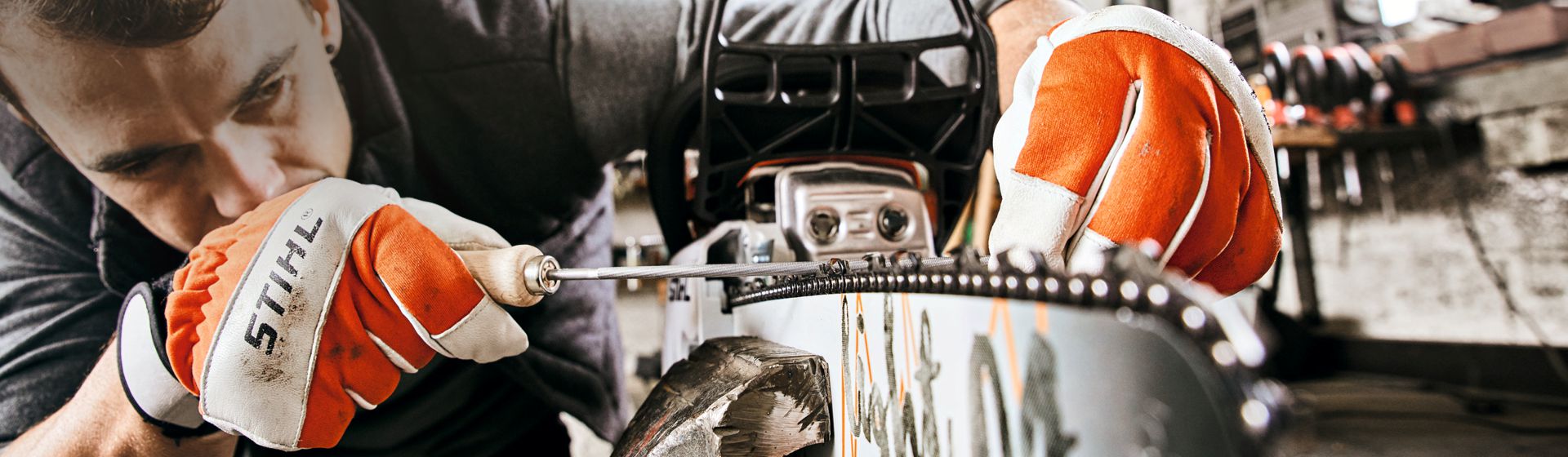 Mann mit Stihl Arbeitshandschuhen beim Bearbeiten einer an eine Motorsäge montierte Sägekette bild
