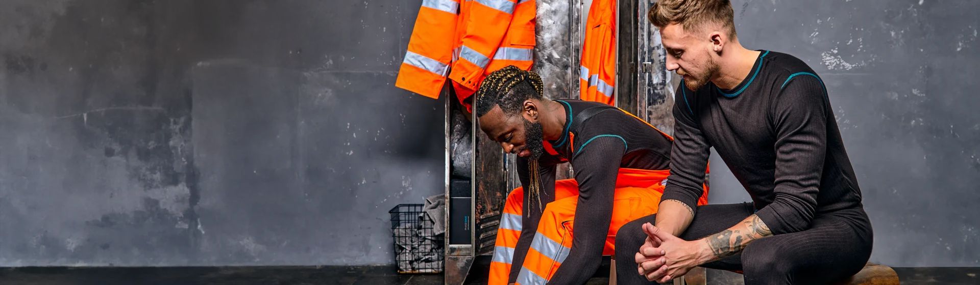 Zwei junge Männer, die schwarze Funktionsunterwäsche tragen, auf einer Umkleidebank sitzend bild
