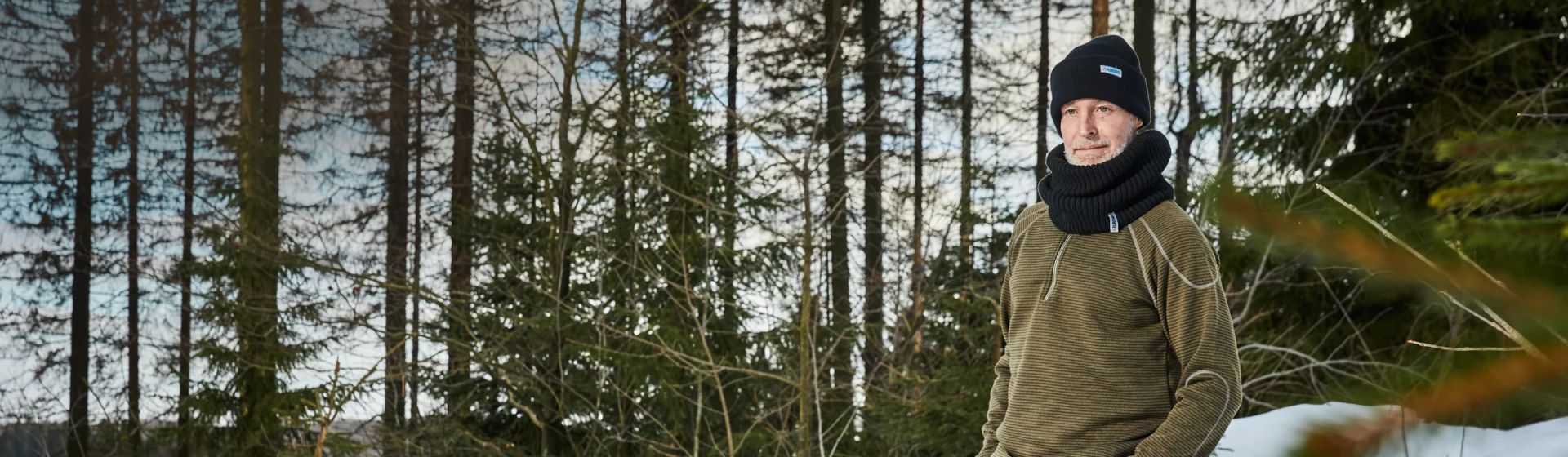 Ein Mann mit schwarzem Schal und schwarzer Wollmütze im winterlichen Wald bild