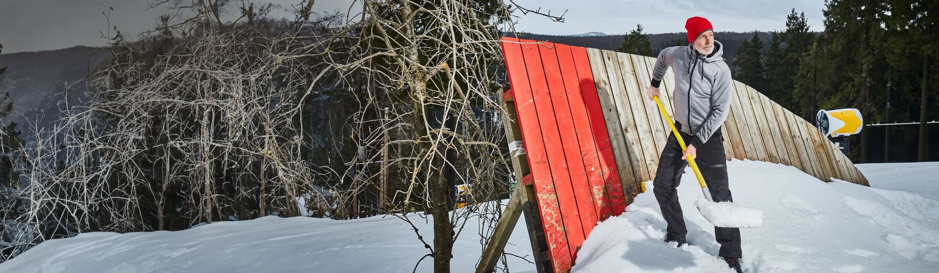 Mann in einer grauen Sweatjacke mit roter Woll-Mütze beim Schneeschippen bild