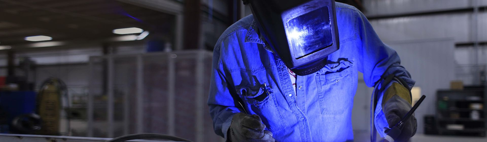 Schweißer in einem blauen Arbeitsoverall mit Schutzhandschuhe und Schutzvisier bei der Arbeit bild