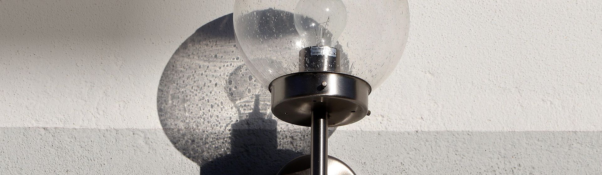 Wandleuchte mit rundem Lampenschirm aus Glas an einer weißen Hauswand hängend bild