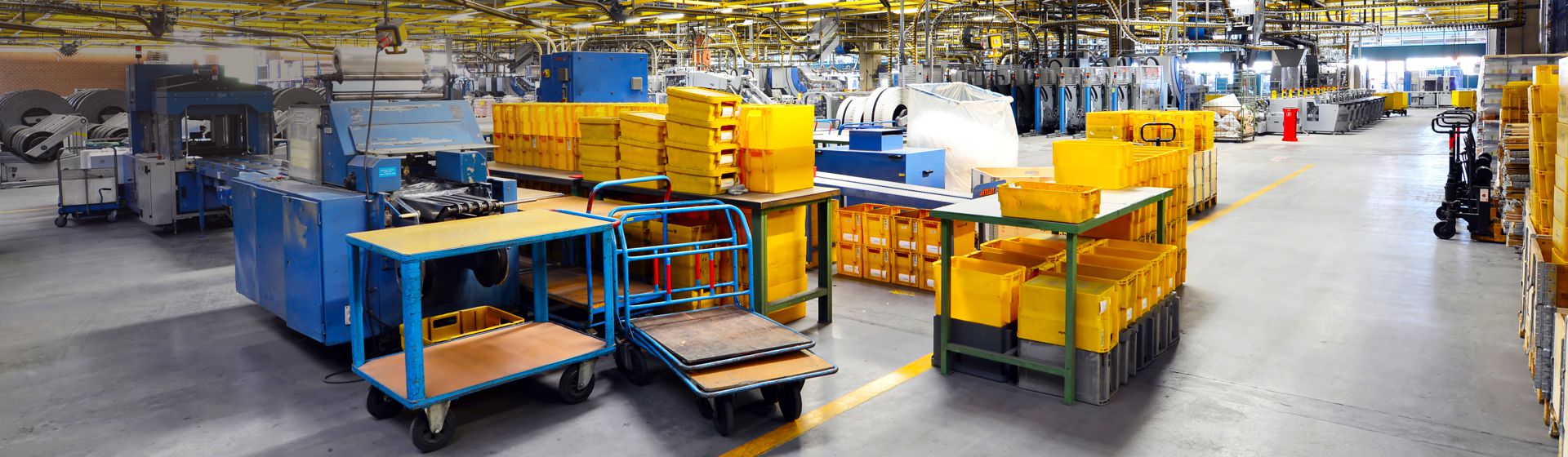 Blick in die Produktion eines Unternehmens, zu sehen sind Maschinen, gelbe Postbehälter, Transportwagen und Hubwagen bild