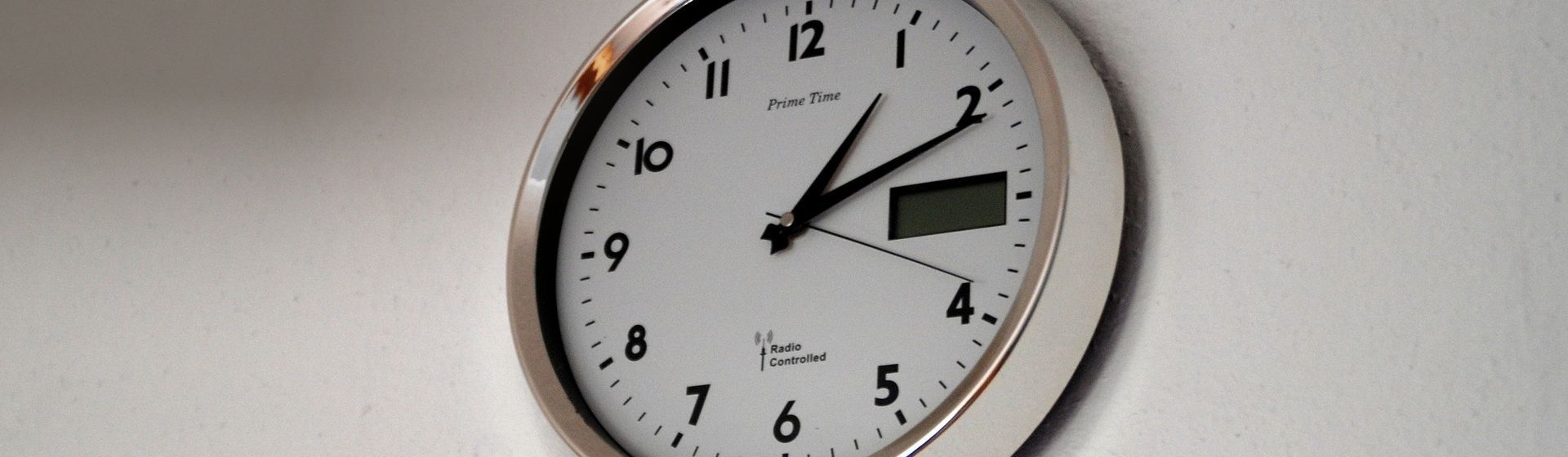 Wanduhr mit weißem Ziffernblatt und silbernem Rahmen an einer hellen Wand montiert bild