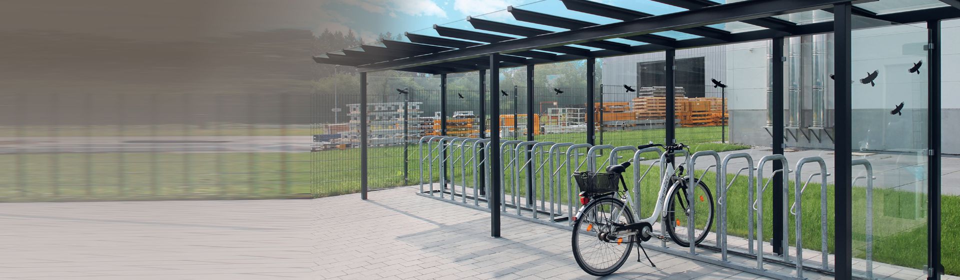 Überdachter WSM Fahrradständer mit einem weißen Damenrad vor einem Firmengebäude in einer industriellen Umgebung bild