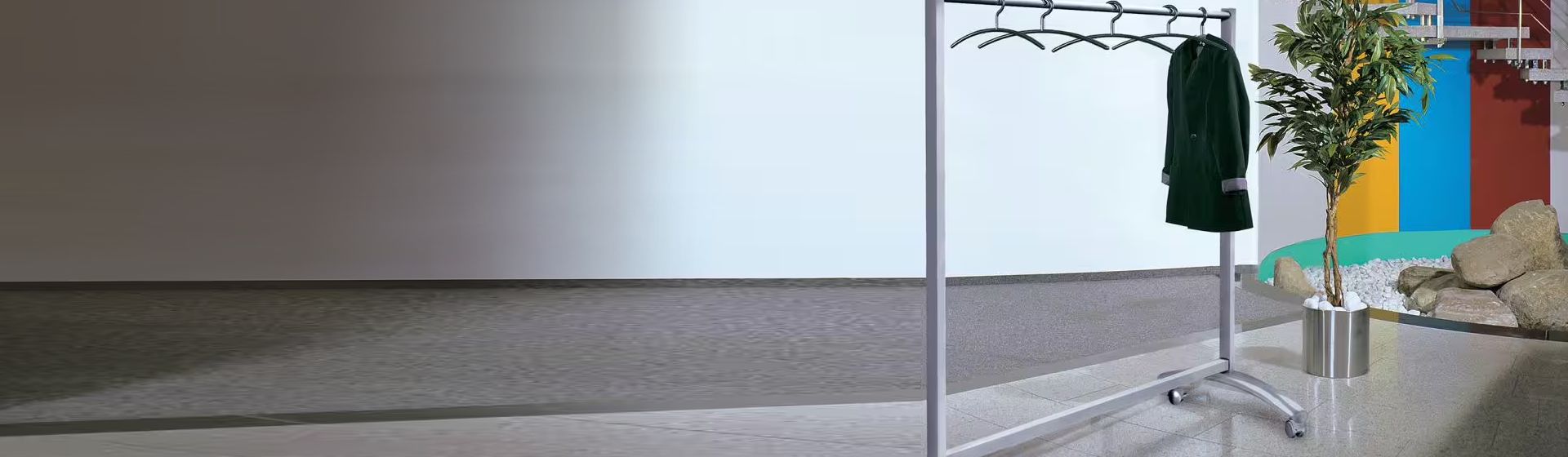 Silberfarbener Garderobenständer mit Kleiderbügeln bestückt, an dem eine grüne Damenjacke hängt, in einer Eingangshalle stehend bild