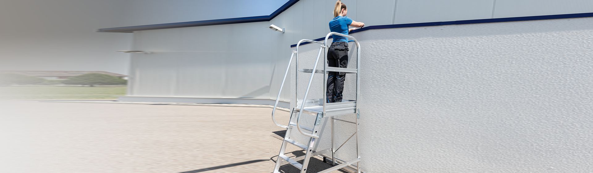 Handwerkerin auf einer Munk Plattformleiter bei Arbeiten an der Außenseite eines Gebäudes bild