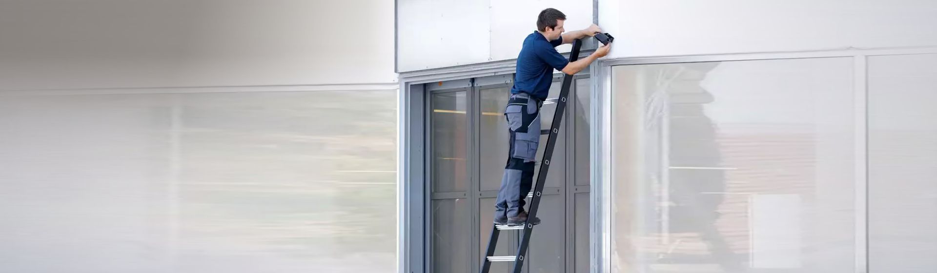 Handwerker bei Montagearbeiten auf einer an einer Fensterfront angelehnten Schwerlastleiter bild