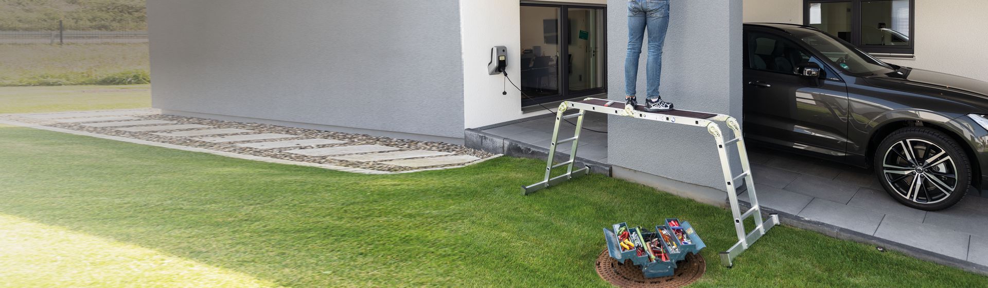 Mann auf einer Munk Vielzweckleiter auf einer Rasenfläche vor einer Garage bild