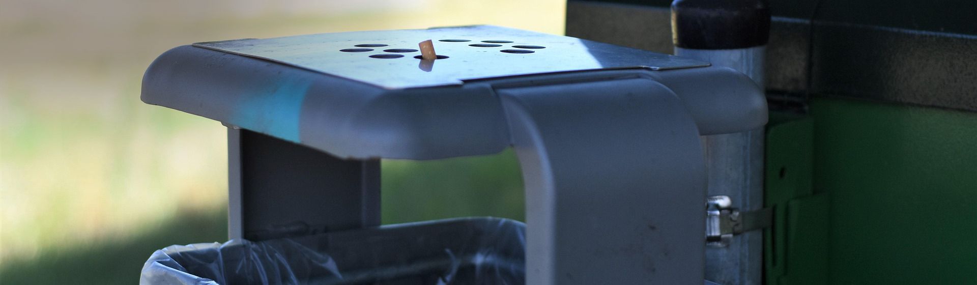 Grauer Abfalleimer mit Ascher, in dem eine ausgedrückte Zigarette steckt bild