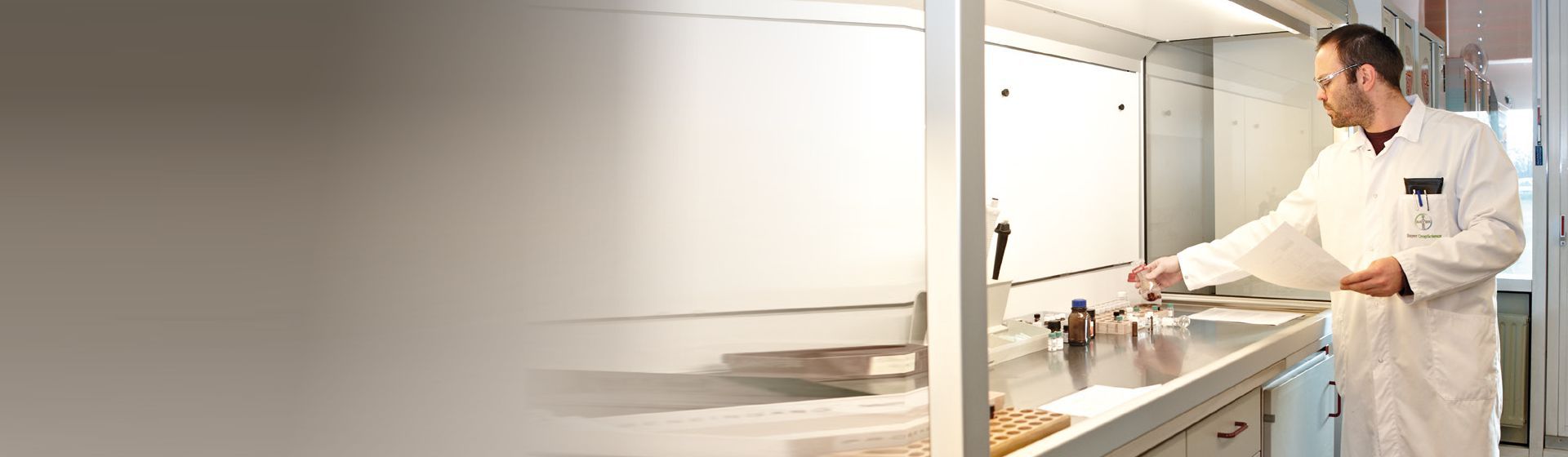 Mann mit Schutzbrille und weißem Arbeitskittel an einem Gefahrstoffarbeitsplatz bild