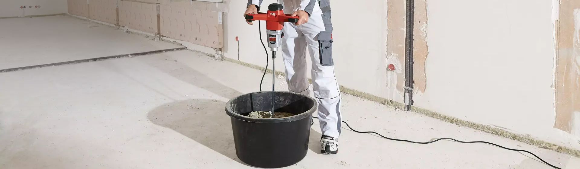 Handwerker mit einem Flex Rührwerk beim Anmischen von Beton in einem Eimer auf einer Baustelle bild