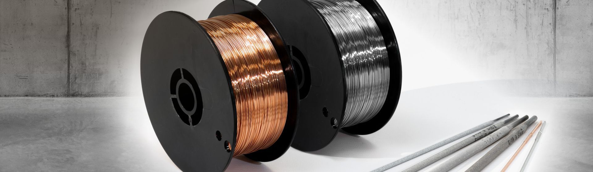 2 Rollen Schweißdraht und diverse Schweißstäbe auf einer grauen Fläche liegend bild