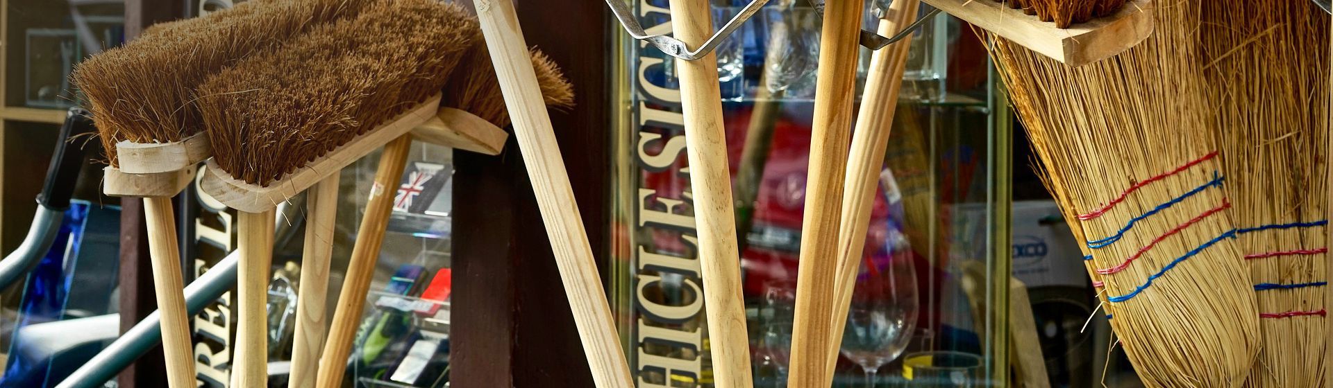 Mehrere Holzbesen zusammen in einem Verkaufsständer vor einem Ladengeschäft bild