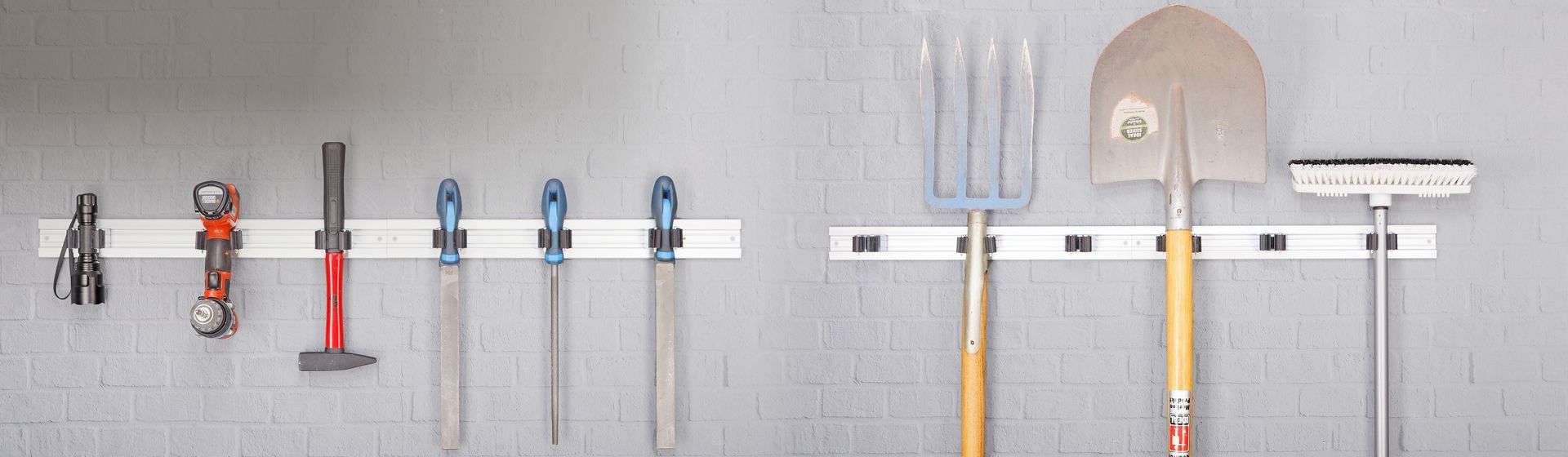 Diverse Garten- und Handwerkzeuge an einem an einer grauen Mauer montierten Gerätehalter hängend bild