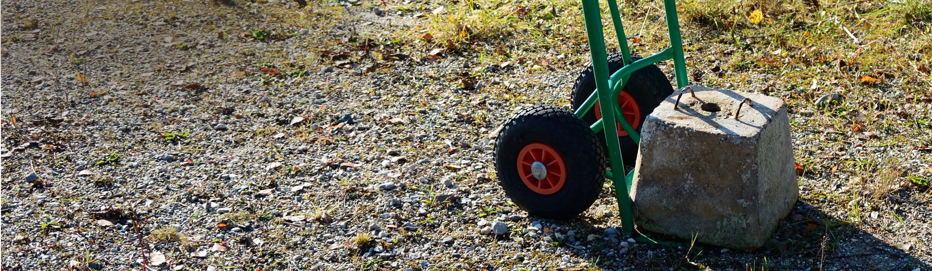 Grüne Sackkarre beladen mit einem Betonklotz auf einem Kieselsteinweg stehend bild