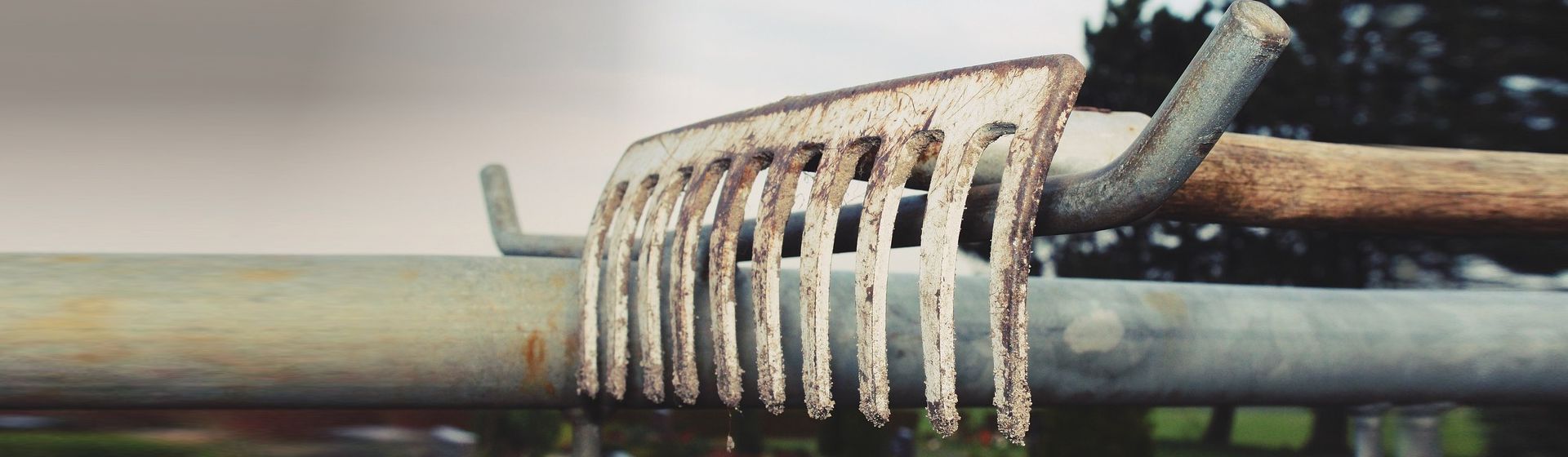 Auf einem Zaun liegender Rechen bild