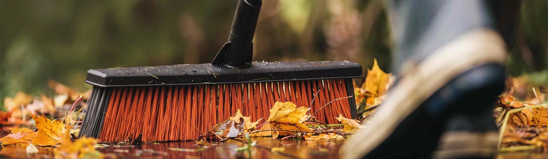 Schwarzer Kehrbesen von Fiskars mit roten Borsten beim Wegfegen von Herbstlaub bild