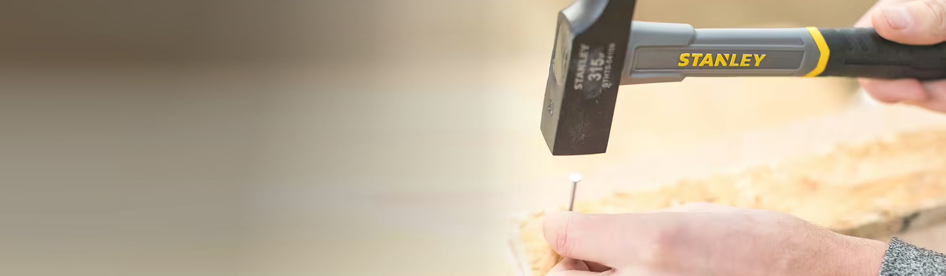 Ein Nagel gehalten mit einer Hand wird mit einem Schreinerhammer von Stanley in ein Holzbrett geschlagen bild