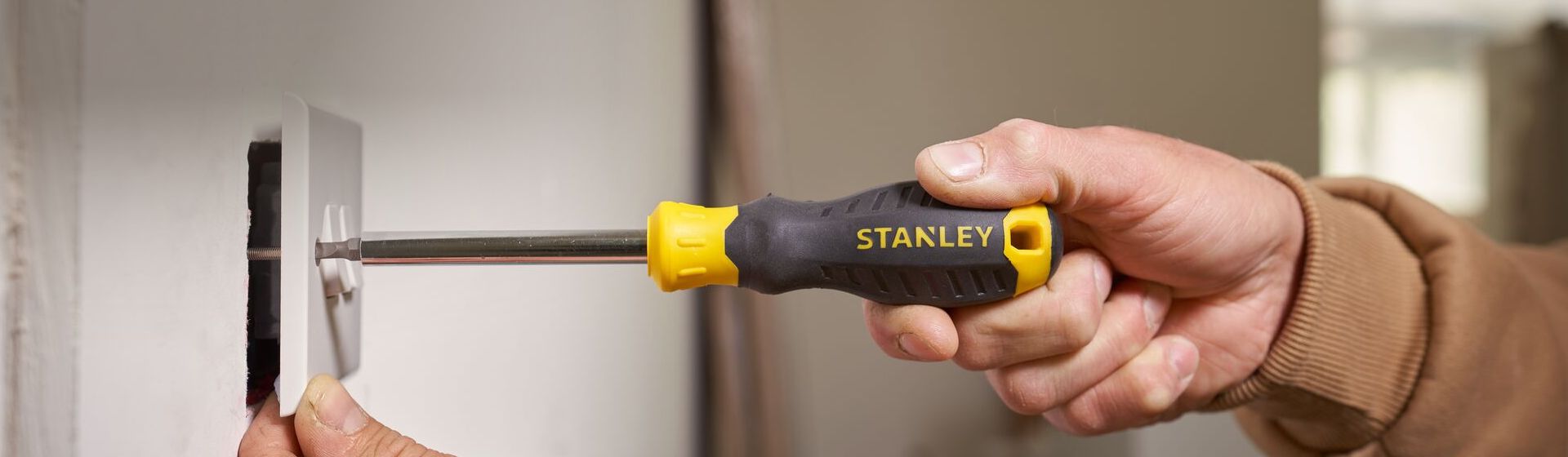 Handwerker befestigt eine weiße Schalterabdeckung mit einem Schlitz-Schraubendreher von Stanley bild