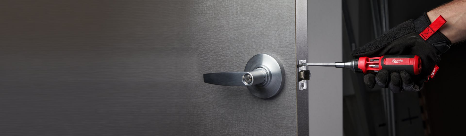 Handwerker befestigt einen Schliesser an der Seite einer grauen Tür mit einem Wechselklingen Schraubendreher von Milwaukee bild