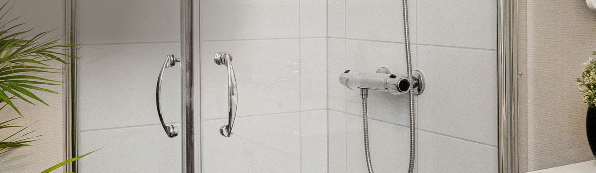 Blick auf eine silberfarbene Thermostatbatterie in einer weiß gefliesten Dusche bild