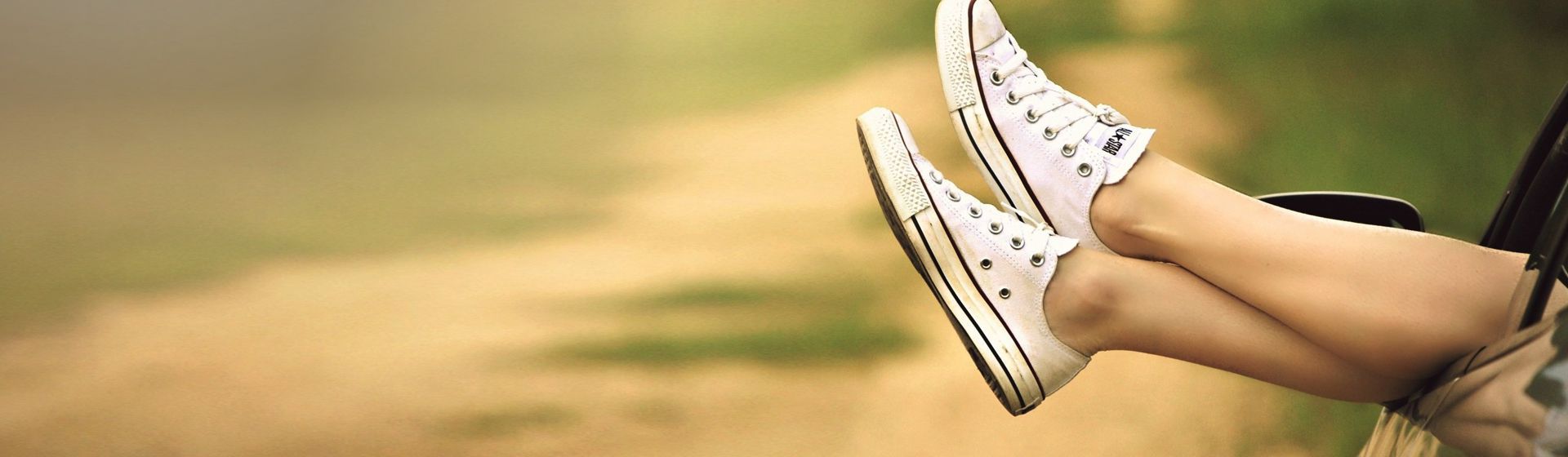 Weibliche Beine mit weißen Sneakern an den Füßen, die aus einem offenen Autofenster hinausgestreckt werden bild